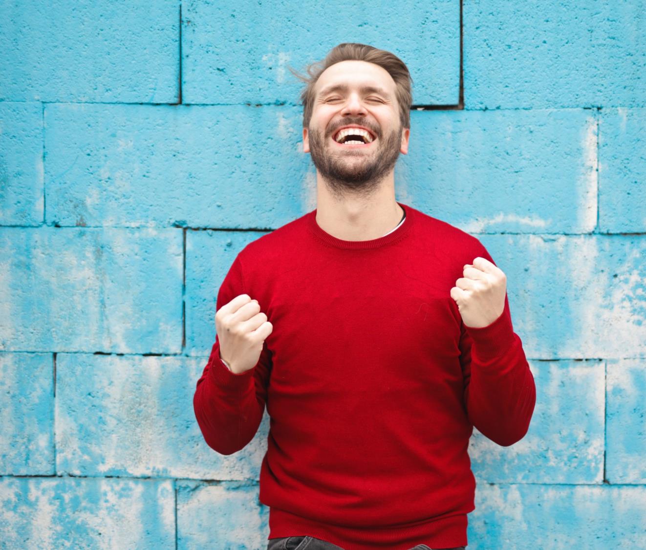 Persona celebrando frente a una pared azul
